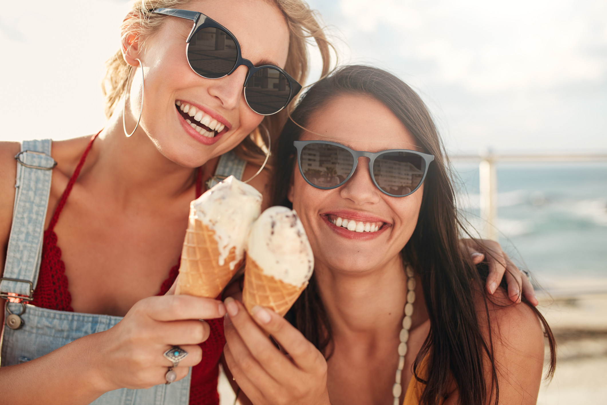 Two young friends having ice cream outside Shot of two young friends enjoying ice cream together on a summer day outdoors. Close up of cheerful female buddies eating icecream.